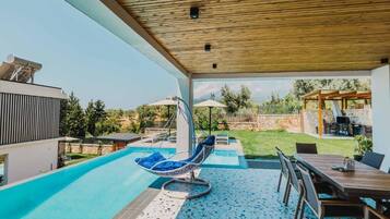 Un espacio exterior techado con piscina, una silla colgante y una mesa de comedor.