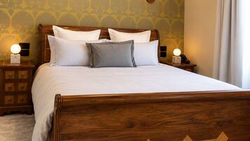 A hotel room with a large wooden bed, two bedside tables, a wall clock, and a patterned wallpaper.