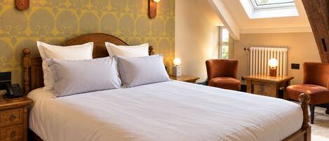 A bedroom with a large bed, two bedside tables with lamps, a wooden chair, and a skylight.