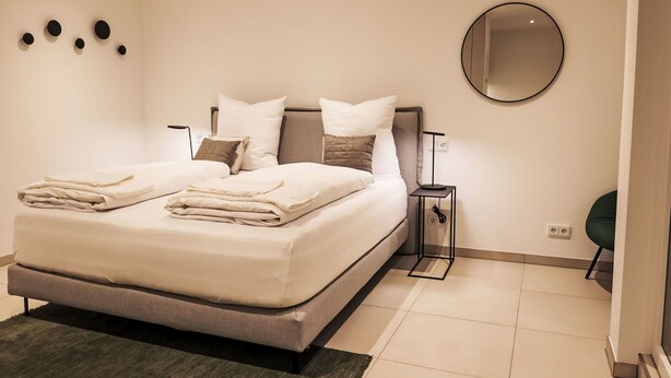 A modern bedroom with a large bed, a bedside table, a round mirror, and a wall-mounted light fixture. - Munich Finest Apartments Studio 11 by Interhome (Munich)
