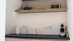 A kitchen with a black countertop, a kettle, a toaster, a coffee maker, and a shelf with a pot and a sign. - Munich Finest Apartments Studio 11 by Interhome (Munich)