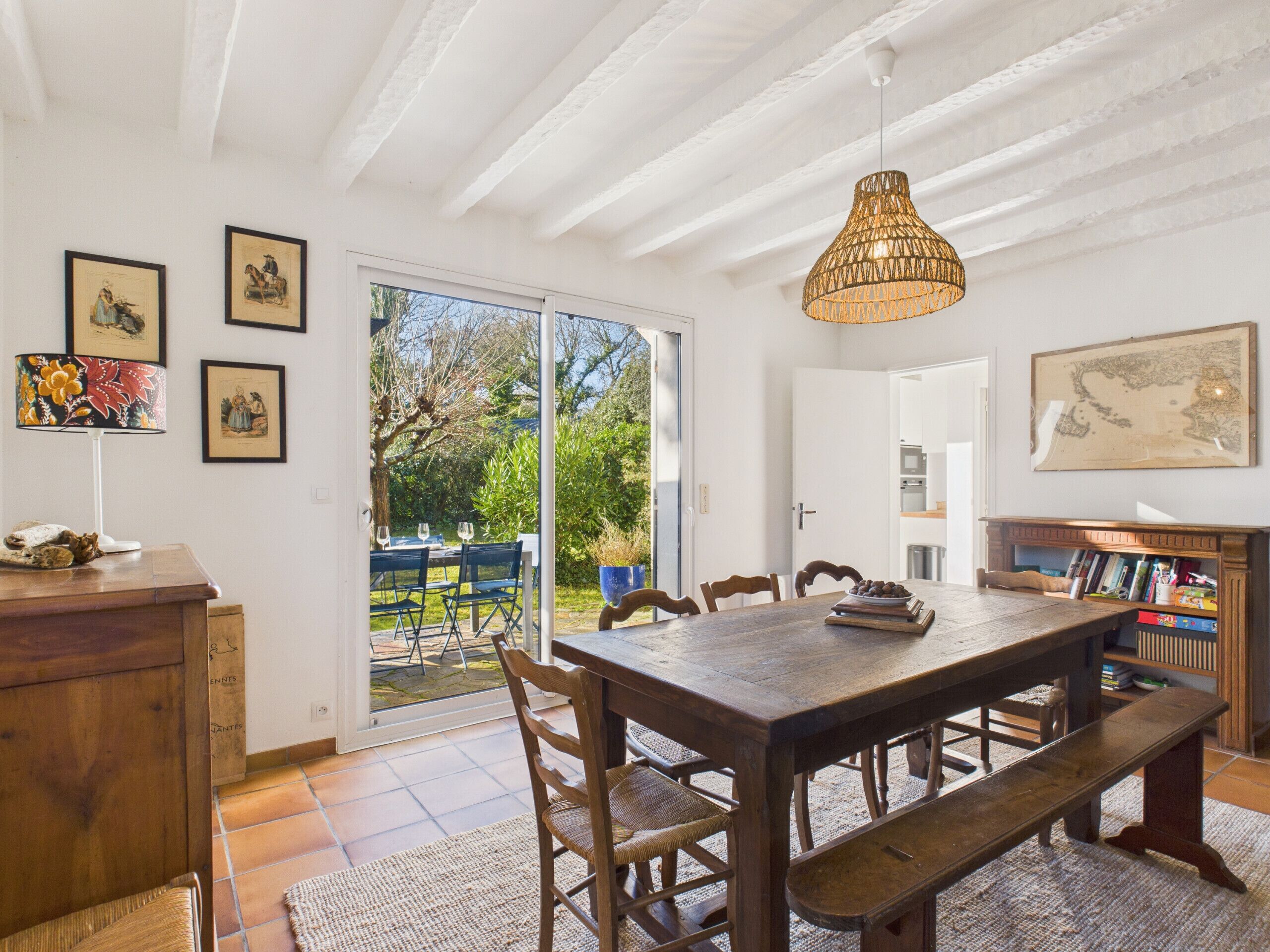 Un área de comedor con una mesa de madera, bancos y sillas. Hay cuadros en la pared, una lámpara y un mapa.