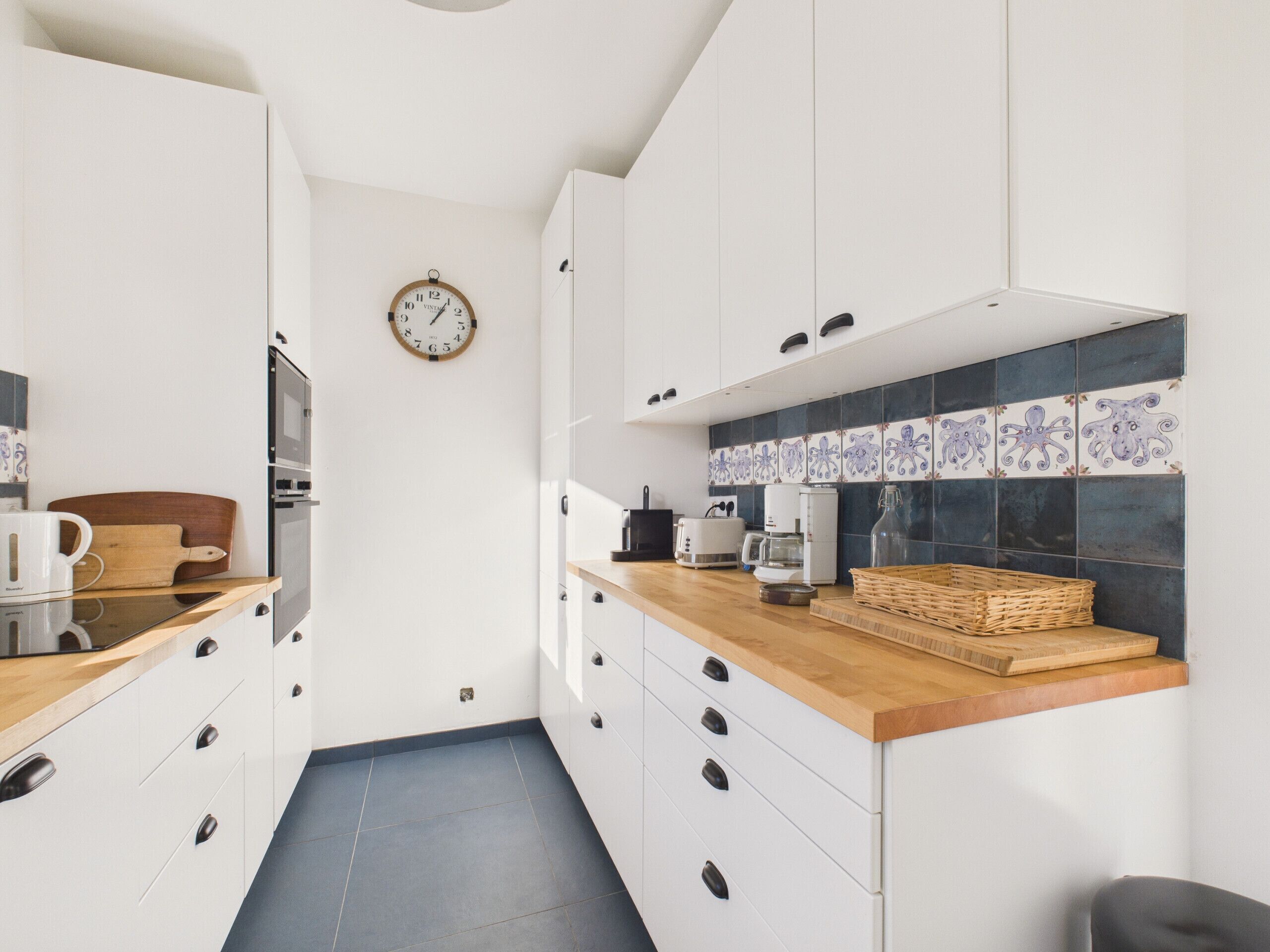 Una cucina moderna con mobili bianchi, un piano di lavoro in legno e uno schienale rivestito di piastrelle blu.