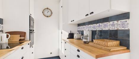 A modern kitchen with white cabinets, a wooden countertop, and a blue tiled backsplash.