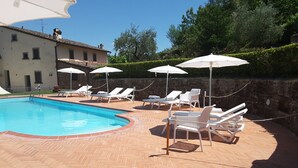 A swimming pool with lounge chairs and umbrellas, surrounded by a brick patio and stone walls. - Old Style Apartment in Florence in Residence with shared pool (Tavarnuzze)