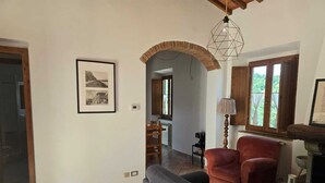 A living room with a fireplace, a red armchair, a grey sofa, and a framed photograph on the wall. - Old Style Apartment in Florence in Residence with shared pool (Tavarnuzze)
