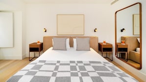 Une chambre d’hôtel avec un grand lit, deux tables de chevet, un miroir et une œuvre d’art encadrée au mur.