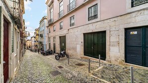 Une rue pavée, bordée de bâtiments des deux côtés, dont certains sont dotés de balcons et de volets.