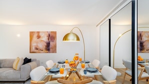 Un espace de salle à manger moderne avec une table à plateau en verre, des chaises blanches et un luminaire suspendu doré.