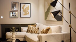 Ein modernes Wohnzimmer mit einem Ecksofa, einem kleinen Beistelltisch mit einer Vase und abstrakter Kunst in Bilderrahmen an der Wand.