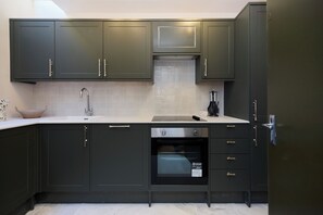 A modern kitchen with dark cabinets, a stainless steel sink, and a built-in oven. - Three-Bedroom Flat on Porchester Square (London)