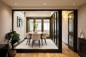 A modern dining area with a wooden table and chairs, a potted plant, and a view into another room. - Three-Bedroom Flat on Porchester Square (London)