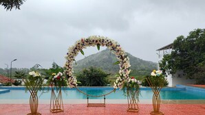 Ein Brautbogen im Freien mit Blumenschmuck, ein Schwimmbad und eine Bergkulisse.