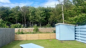 Un patio trasero con una mesa y bancos de picnic de madera, un cobertizo y una cerca de madera.