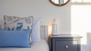 Un dormitorio con una cama, almohadas, una mesita de noche, una lámpara y un espejo en la pared.
