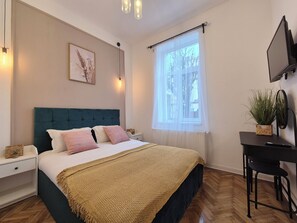 A bedroom with a bed, bedside tables, a desk, a chair, a potted plant, and a window with sheer curtains. - Central Inn Brasov (Brașov)