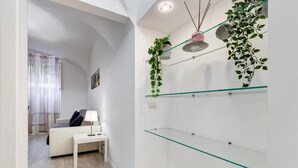 Una sala de estar moderna con un sofá blanco, una mesita con una lámpara y estantes de vidrio con plantas.