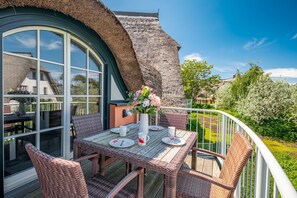 A balcony with wicker furniture, a table set for two, and a large window. - Maisonette apartment on the Baltic Sea beach (Dierhagen)
