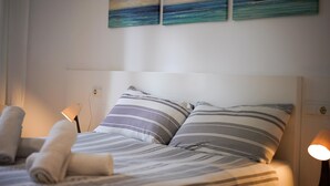 A neatly made bed with striped bedding, two pillows, and rolled towels on the side. There are two wall-mounted lamps on either side of the bed. - Nice apartment for two people in Cala Sant Vicenç (Cala Sant Vicenç)