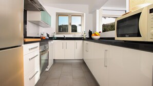 A modern kitchen with white cabinets, a black countertop, and a microwave. There is a window above the sink, and a view of the outdoors is visible. - Nice apartment for two people in Cala Sant Vicenç (Cala Sant Vicenç)