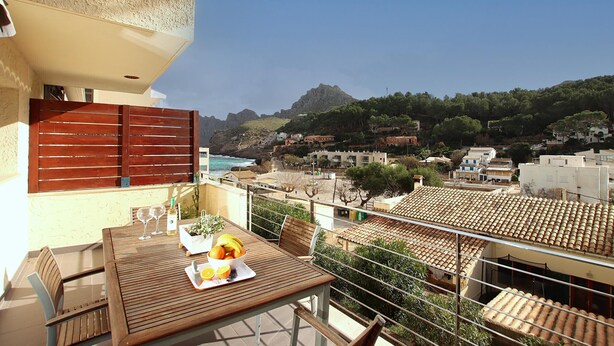 A balcony with a wooden table set for two, overlooking a coastal town with terracotta rooftops and a mountain in the distance. - Nice apartment for two people in Cala Sant Vicenç (Cala Sant Vicenç)