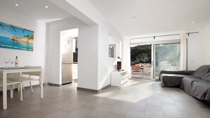 A spacious living area with a dining table, chairs, a sofa, and a kitchen in the background. - Nice apartment for two people in Cala Sant Vicenç (Cala Sant Vicenç)