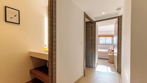Corredor que leva a um quarto com cama, mesa de cabeceira e janela.