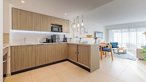 Cozinha moderna com armários de madeira, micro-ondas e máquina de café. Há uma área de refeições com mesa e cadeiras, e uma grande janela com cortinas.