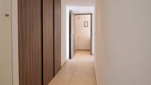 Corredor com armários de madeira e piso de azulejos, que leva a um banheiro com vaso sanitário e um quadro na parede.