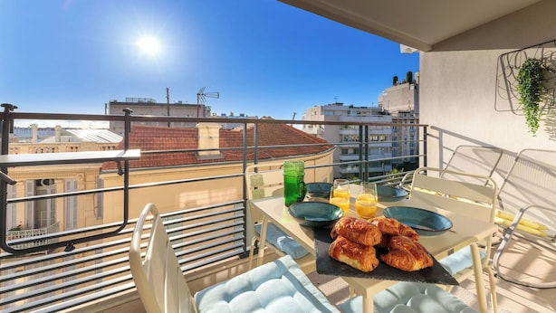Varanda com mesa posta para o café da manhã, incluindo croissants e suco de laranja, com vista para a cidade.