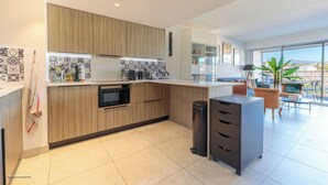 A modern kitchen with wooden cabinets, a microwave, and a coffee maker. There is a small trash bin and a grey storage unit. The kitchen leads to a balcony with a view of the city. - Apartment in Cannes with 1 bedrooms sleeps 4 (Cannes)