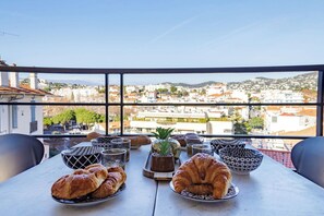 Mesa com croissants e tigelas em uma varanda com vista para a paisagem urbana.