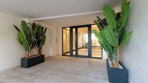 Un hall spacieux doté d’un sol carrelé, de deux grands plants en pot et d’une porte coulissante en verre donnant sur une autre pièce.