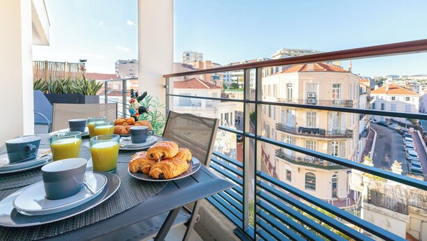 Un balcon aménagé pour le petit-déjeuner, avec des croissants, du jus d’orange et des tasses à café.