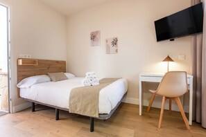 Quarto de hotel com uma cama, uma mesa, uma cadeira, uma televisão e obras de arte na parede.