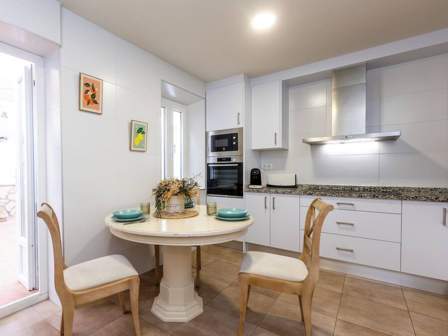 A kitchen with white cabinets, a central island with chairs, a microwave, oven, and a toaster.