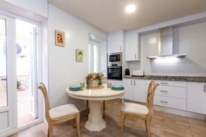 Una cocina con gabinetes blancos, una isla central con sillas, microondas, horno y tostadora.