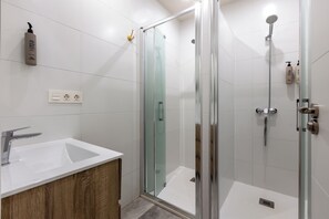 Un baño moderno con ducha envuelta en vidrio, lavamanos blanco y tocador de madera.