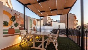 Una terraza en la azotea con una mesa y sillas de madera, una planta en maceta y un mural en la pared.