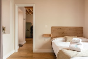 A bedroom with a wooden headboard, a bedside shelf, a bed with white linens, and a small bedside table. - Hospedería Boho Granada by eme hoteles (La Zubia)