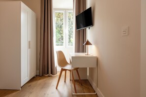 Una habitación con escritorio, silla, televisor y ventana con cortinas.