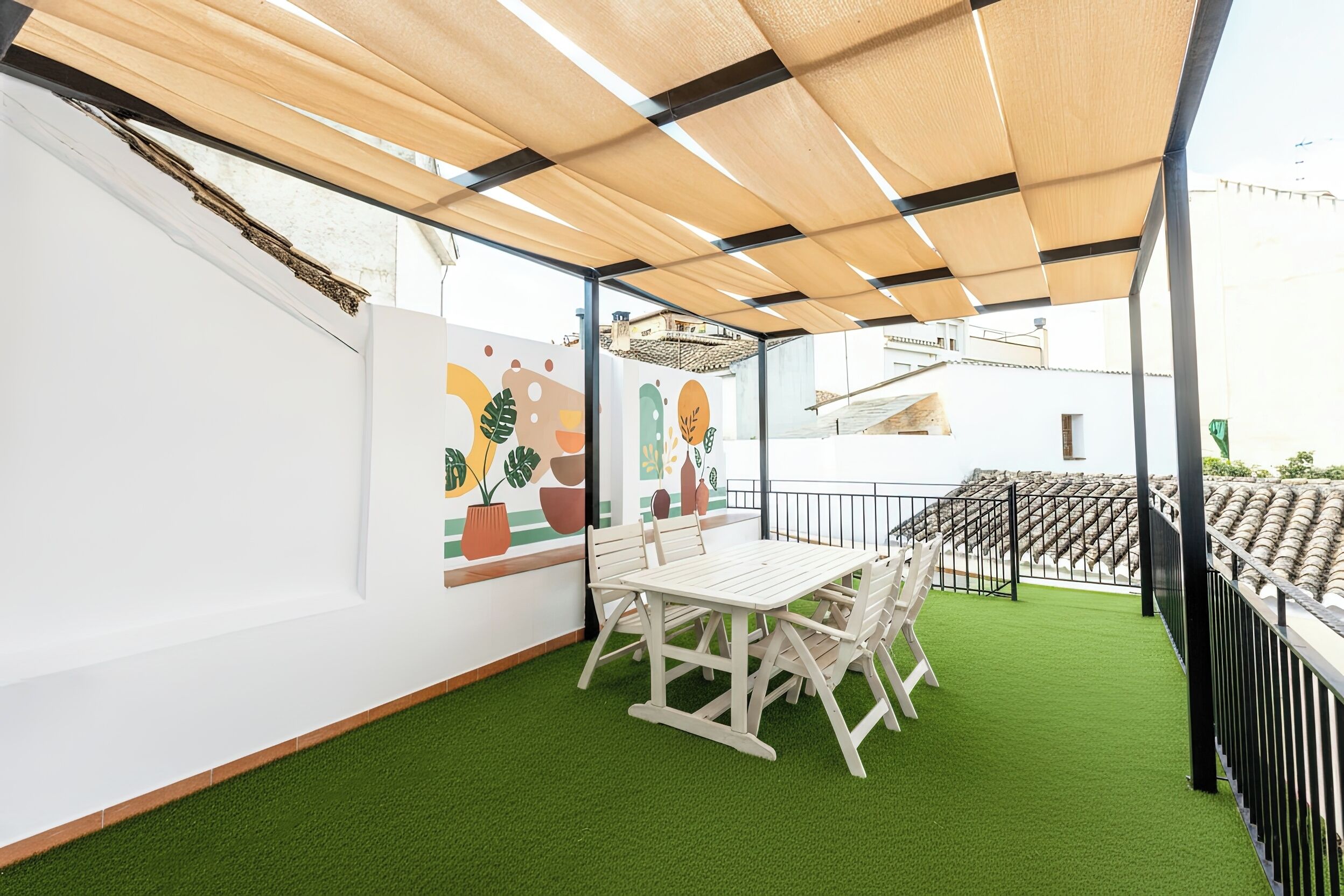 An outdoor seating area with a table and chairs, a wooden pergola, and a green artificial turf floor.