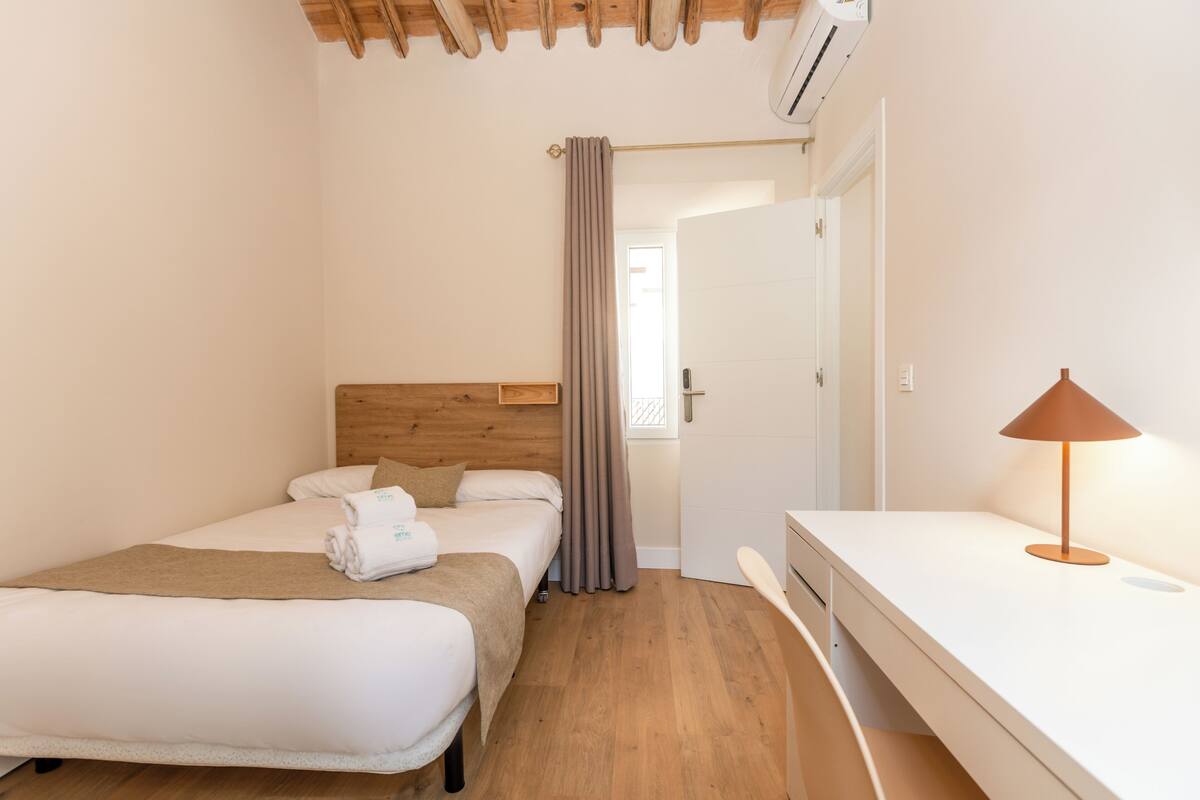 Ein Hotelzimmer mit zwei Betten, einem hölzernen Kopfteil, einem Schreibtisch mit Lampe und einer Tür zu einem weiteren Raum.