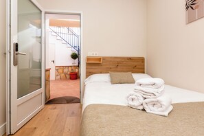 Habitación de hotel con cama, cabecero de madera, repisa montada en la pared, planta en maceta y puerta que da a una escalera.
