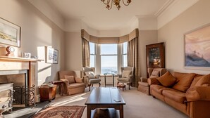 A spacious living room with a large window, a fireplace, and a view of the ocean.