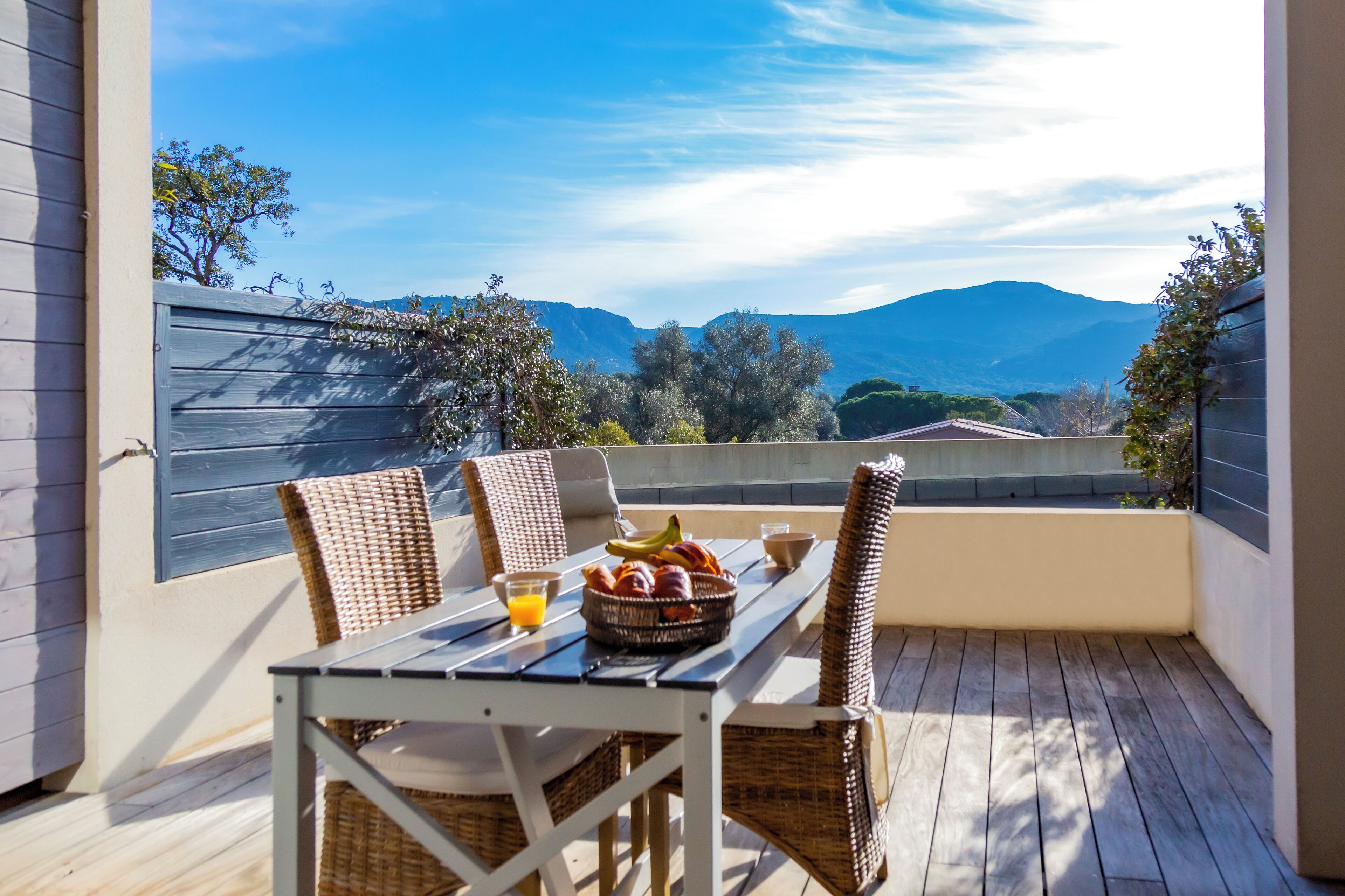 A balcony with wicker chairs, a table, and a fruit bowl with a glass of orange juice.