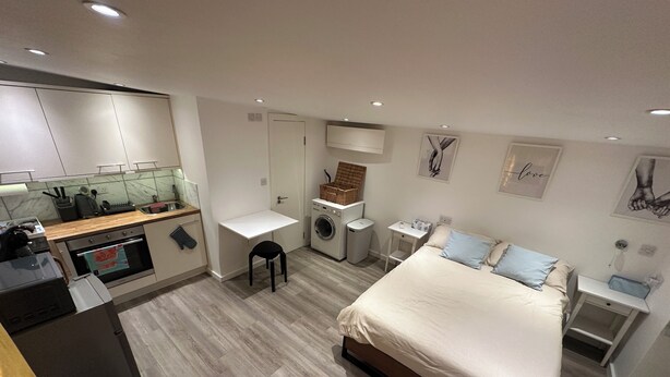 Een compacte hotelkamer met een kitchenette, een klein bureau, een bed en een wasmachine.