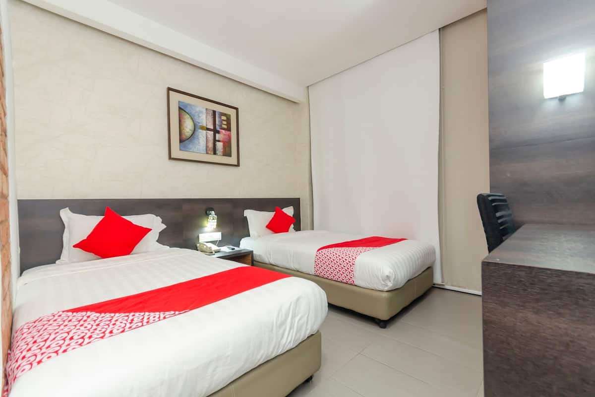 Une chambre d’hôtel avec deux lits, une table de chevet, une lampe, un tableau encadré au mur et une chaise.