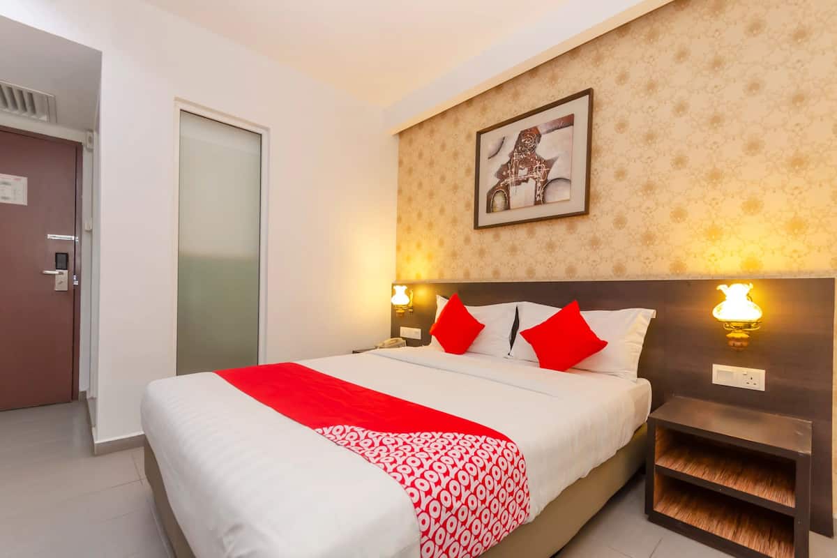 Une chambre d’hôtel avec un lit, une table de chevet, une lampe fixée au mur, une porte et un tableau encadré accroché au mur.