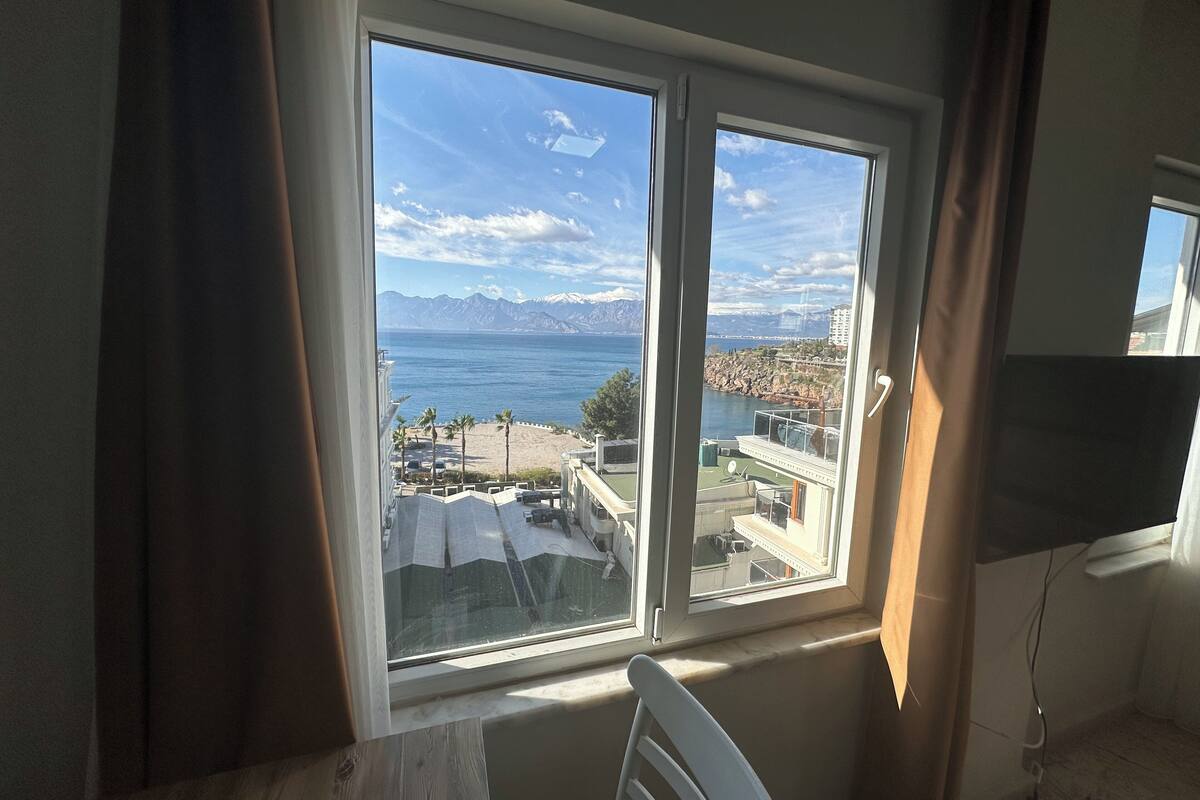 A room with a large window offering a view of a beach, mountains, and a cityscape.